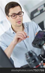 young confident technician is fixing and cleaning a digital cameralense