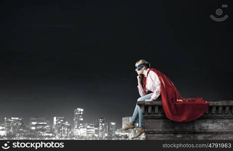 Young confident woman in red cape and mask. She is super woman