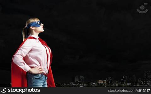 Young confident woman in red cape and mask. She is super woman