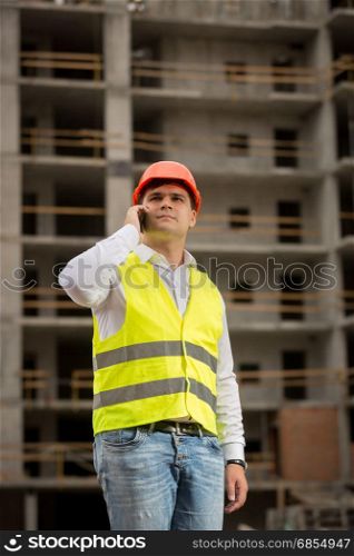 Young construction engineer talking by phone on building site