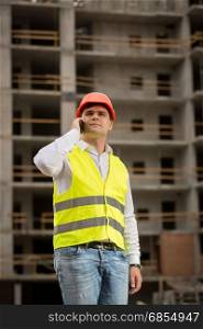 Young construction engineer talking by phone on building site