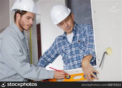 young construction worker with colleague checking the level