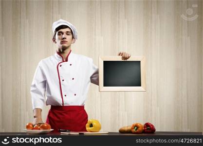 Young cook. Handsome cook holding blank chalk board. Place for text