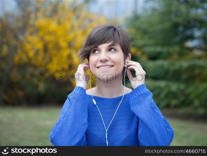 Young cool girl dressed in blue in the park listening music with earphones