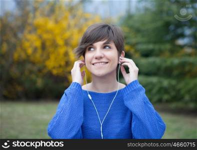 Young cool girl dressed in blue in the park listening music with earphones