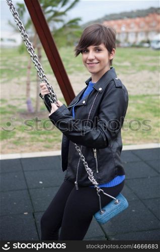 Young cool girl with leather jacket sitting on a swing