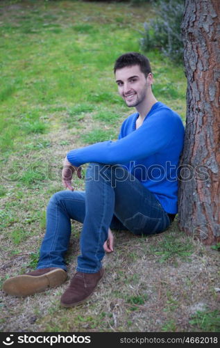 Young cool man in the park sitting next a tree