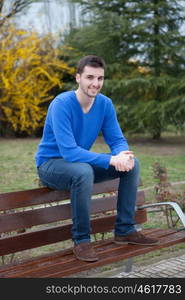 Young cool man reading a book sitting on a bank in the park