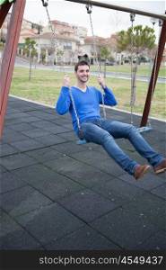Young cool man sitting on a swing in the park