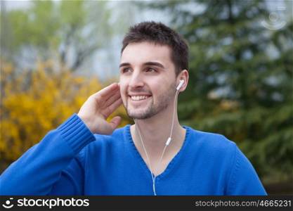 Young cool men dressed in blue in the park listening music with earphones