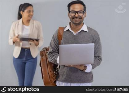 Young corporate employee standing with laptop and his colleague standing behind with digital tablet