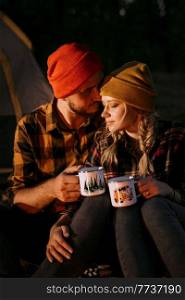 Young couple a guy and a girl in bright knitted hats stopped at a camping near the fire