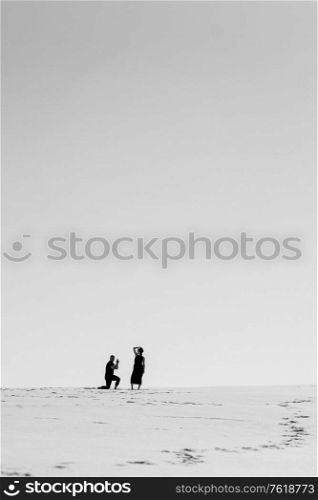young couple a guy and a girl with joyful emotions in black clothes walk through the snow white desert