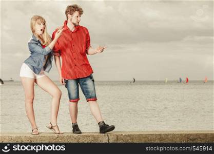 Young couple against sky. Best friends sharing free time looking surprised showing with finger outdoor by seaside