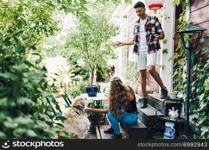 Young couple and their dog sitting smiling in the garden chairs near their wooden house