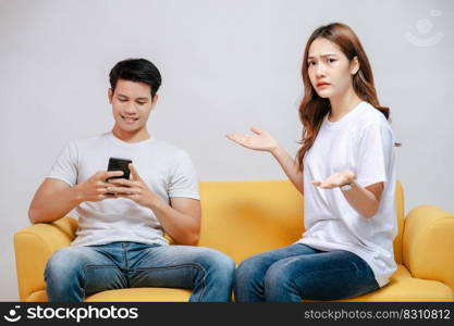 young couple arguing while handsome man using mobile phone on sofa in living room at home. husband addict On Mobile Phone Ignoring her, upset couple, family issues and relationship concept