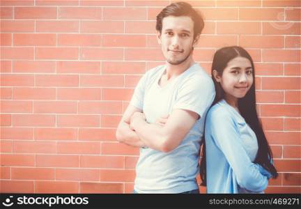 Young couple asian man and woman attractive stand arm crossed and smile while back to back on brick wall background with romantic, boyfriend and girlfriend with confidence, romantic concept.
