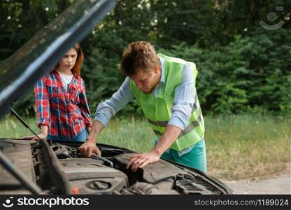 Young couple at the opened hood on road, car breakdown. Broken automobile or emergency accident with vehicle, trouble with engine on highway