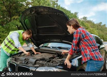 Young couple at the opened hood on road, car breakdown. Broken automobile or emergency accident with vehicle, trouble with engine on highway. Couple at the opened hood on road, car breakdown