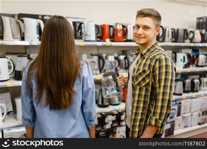 Young couple at the shelf with electric kettles in electronics store. Man and woman buying home electrical appliances in market. Couple at the shelf with electric kettles in store