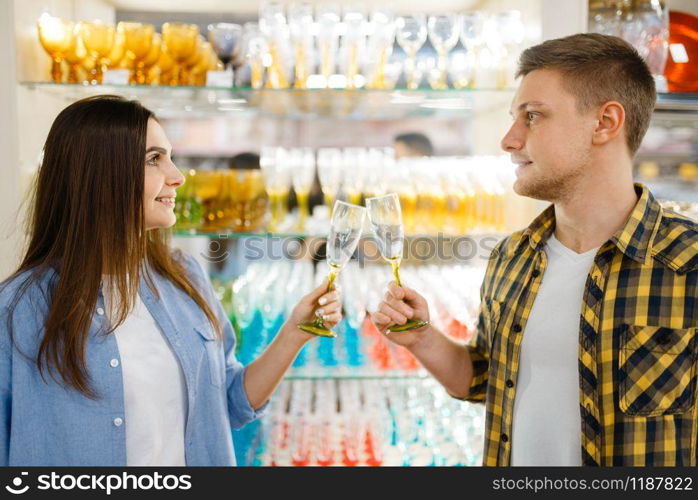 Young couple at the shelf with wineglasses in houseware store. Man and woman buying home goods in market, family in kitchenware supply shop. Couple at shelf with wineglasses, houseware store