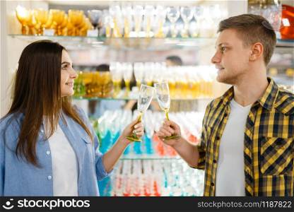 Young couple at the shelf with wineglasses in houseware store. Man and woman buying home goods in market, family in kitchenware supply shop. Couple at shelf with wineglasses, houseware store