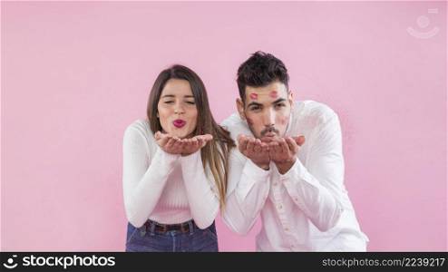 young couple blowing kisses pink background