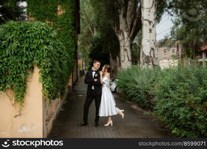 young couple bride and groom in a white short dress walking in the rain