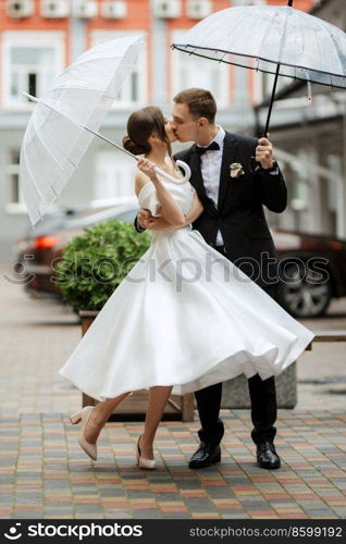 young couple bride and groom in a white short dress walking in the rain