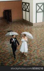 young couple bride and groom in a white short dress walking in the rain