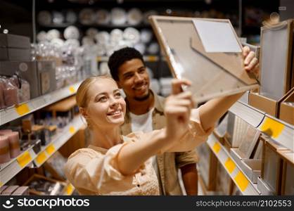 Young couple buying picture photo frame at shop. Multi ethnic woman man choosing decor for housing. Young couple buying photo frame at shop