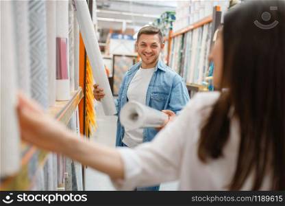 Young couple buying wallcovering in hardware store. Male and female customers look at the goods in diy shop