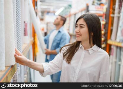Young couple buying wallcovering in hardware store. Male and female customers look at the goods in diy shop. Young couple buying wallcovering in hardware store