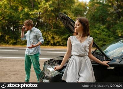 Young couple calling a tow truck on road, car breakdown. Broken automobile or emergency accident with vehicle, trouble with engine on highway