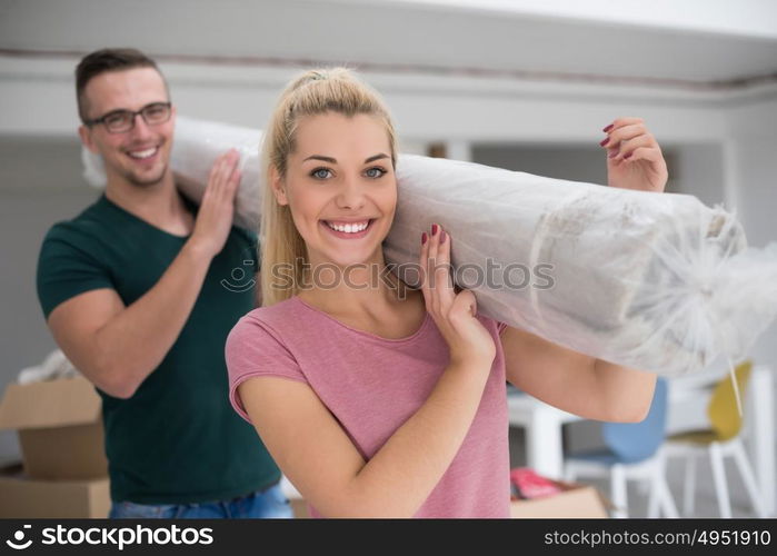 Young couple carrying a carpet moving in to new home together. Home, people, moving and real estate concept