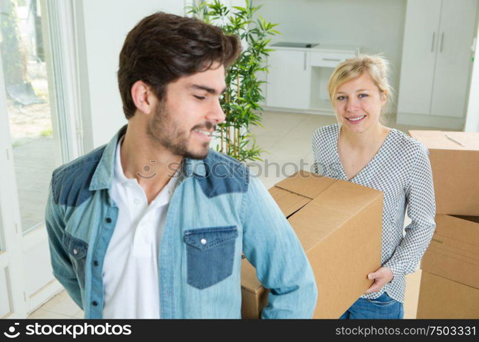 young couple carrying box in apartment