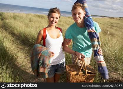 Young Couple Carrying Picnic Basket And Windbreak Walking Through Dunes