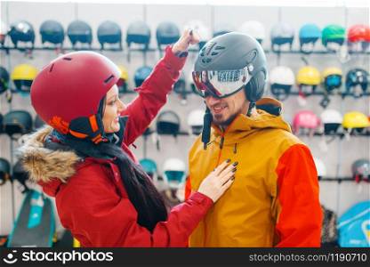 Young couple check the strength of the ski or snowboarding helmet, sports shop. Winter season extreme lifestyle, active leisure store, buyers choosing protect equipment