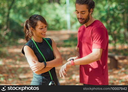 Young couple checking progress on their smart watches after outdoor training. Young couple Looking at Their Smart Watches After Outdoor Training