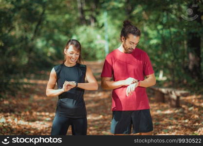 Young couple checking progress on their smart watches after outdoor training. Young couple Looking at Their Smart Watches After Outdoor Training