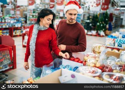 Young couple chooses christmas tree toys in shop, family tradition. December shopping of holiday goods and decorations