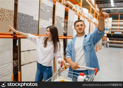 Young couple choosing ceramic tile in hardware store. Male and female customers look at the goods in diy shop