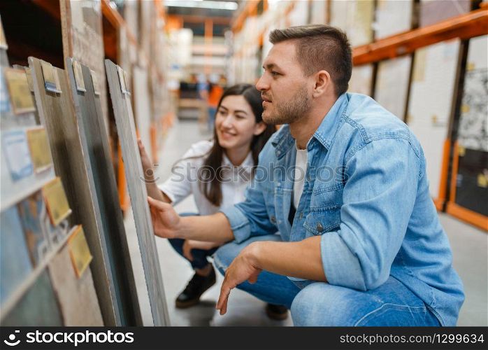 Young couple choosing ceramic tile in hardware store. Male and female customers look at the goods in diy shop. Young couple choosing ceramic tile, hardware store
