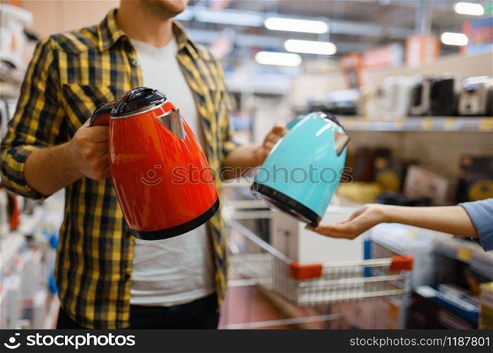 Young couple choosing electric kettle in electronics store. Man and woman buying home electrical appliances in market. Couple choosing electric kettle, electronics store