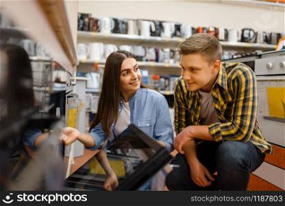 Young couple choosing electric oven in electronics store. Man and woman buying home electrical appliances in market. Couple choosing electric oven in electronics store
