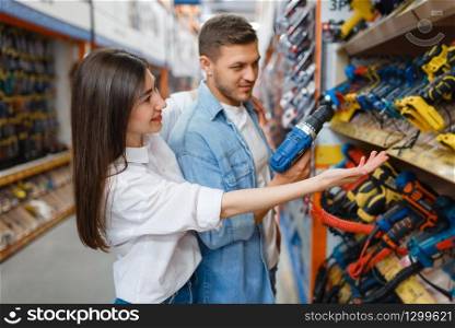 Young couple choosing instrument in hardware store. Male and female customers look at the goods in diy shop