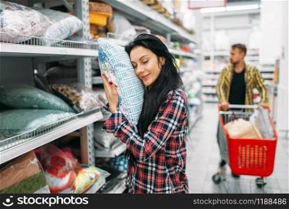 Young couple choosing pillow in supermarket. Male and female customers on family shopping. Man and woman purchasing goods for the house. Young couple choosing pillow in supermarket