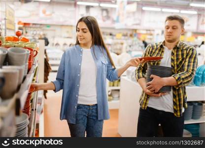 Young couple choosing plates in houseware store. Man and woman buying home goods in market, family in kitchenware supply shop. Young couple choosing plates in houseware store