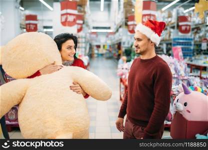 Young couple choosing plush toys on christmas in supermarket, family tradition. December shopping of new year holiday goods and decorations. Young couple choosing plush toys in supermarket