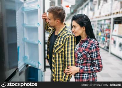 Young couple choosing refrigerator in supermarket. Male and female customers on family shopping. Man and woman purchasing goods for the house